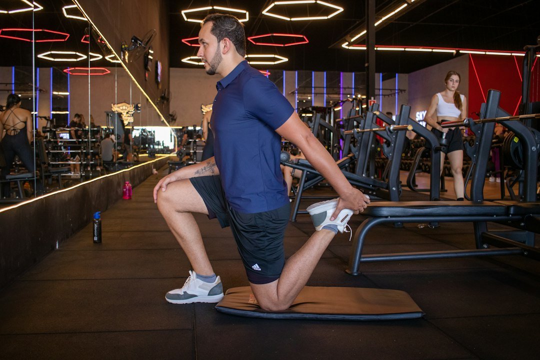 Man stretching quadriceps on a mat in gym