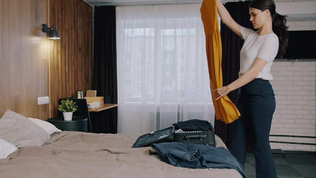 A woman holding a yellow dress while packing a suitcase on a bed
